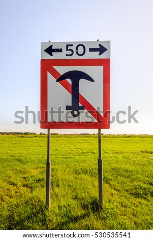 Dutch square prohibition sign to anchor a boat over a distance of 50 meters on either side of the sign. The sign on iron poles is placed on the bank of a wide river in the Netherlands.