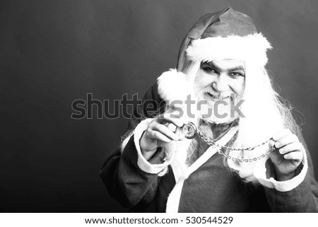 New year man with smiling face has long white beard and hair in santa claus christmas coat and hat holding clock on chain on studio background, black and white, copy space