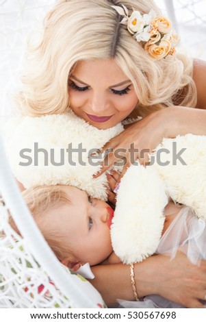 Beautiful mother with a young daughter in her arms. Photographed in a light tone in the interior of a white studio. The beauty of motherhood, family happiness, a woman with white wavy hair