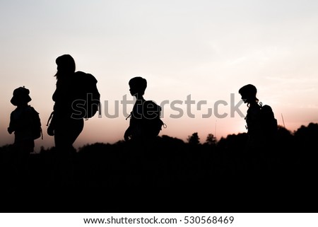 Silhouettes of family hiking at sunset. Happy big family on summer vacation in mountains. Mom and kids carry backpacks. Tourists walking on hill edge. Summertime fun. Little children traveling.