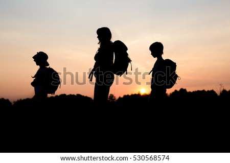 Silhouettes of family hiking at sunset. Happy family on summer vacation in mountains. Mom and kids carry backpacks. Tourists walking on cliff edge. Summertime fun. Little children traveling.