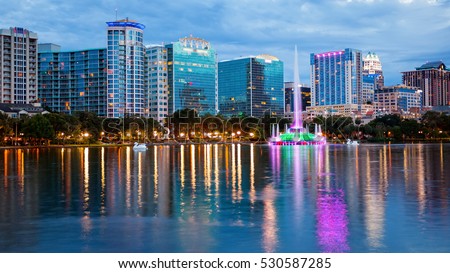 Orlando, Florida city skyline and water fountain at night in Lake Eola Park, building logos blurred for commercial use