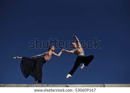 young woman and a man performing gymnastic exercises against the sky