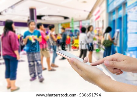 Girl use mobile phone, blur image of people stand in front of the ATM.