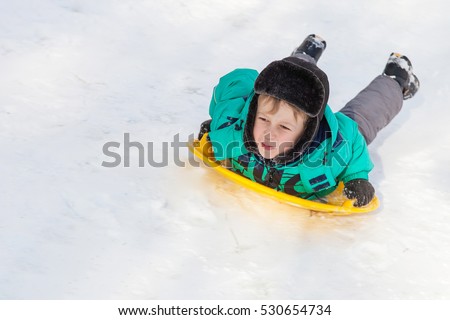 Boy sliding down the hill on saucer sleds outdoors, winter day, ride down the hills, winter games and fun