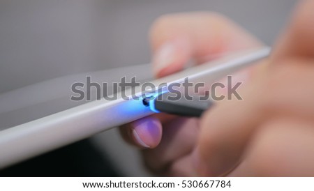 Woman's hand plugging black lightning charging cable into pc digital tablet - USB data cable connecting on modern gadget. Close up