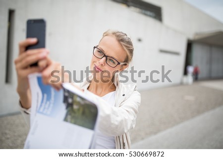 Pretty, female tourist taking a selfie picture while visiting a foreign city and its highlights landmarks, looking happy and relaxed. loving the travel (shallow DOF; color toned image)