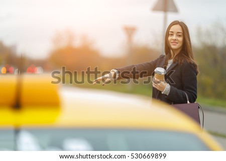 Happy girl with coffee in hand stops yellow taxi