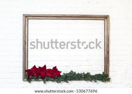Wooden picture frame with a branch of pine-tree and red flower on a white brick background