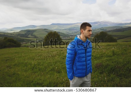 handsome Man looking into the distance, beautiful mountains in the background, thinking deeply, wearing blue jacket, nature, slow life, traveling 