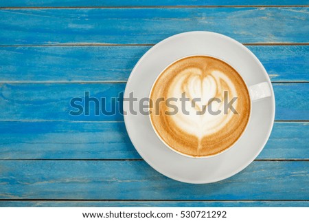 Top view hot latte coffee in white cup on blue vintage wooden table background.