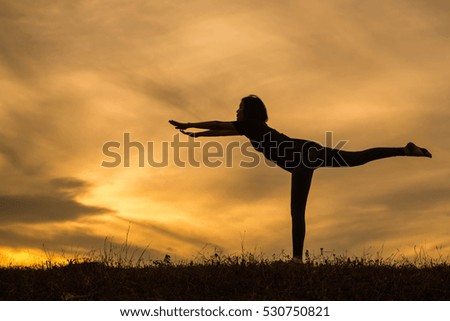 Silhouette of Beautiful Woman practicing yoga on lawn at sunset