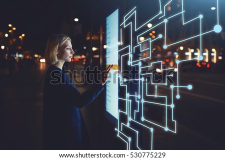 Young woman touching sensitive screen while selecting surface option. Female standing at big display with advanced innovative device with infographics design elements.Person with futuristic technology Royalty-Free Stock Photo #530775229