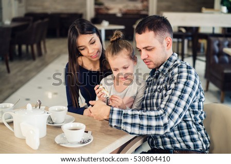 family, parenthood, technology people concept - happy mother, father and little girl having dinner taking selfie by smartphone at restaurant