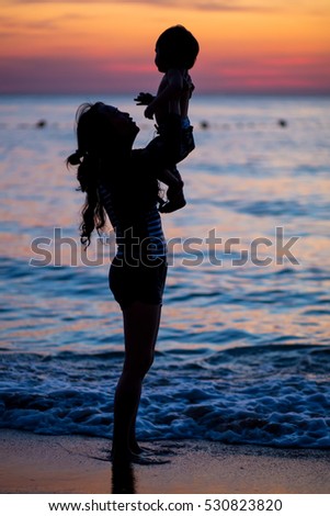 Silhouettes mother and son playing on the beach at the dawn time. Concept of family.