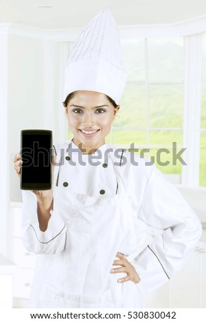 Picture of female chef showing mobile phone with empty screen in the kitchen