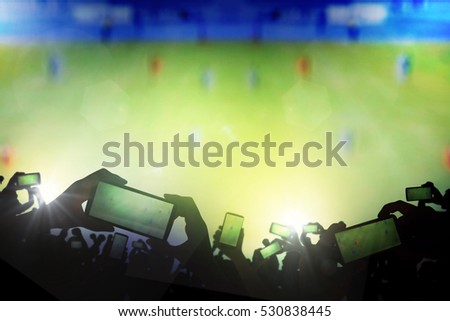 Silhouette of hands using smart phone to take pictures and videos at live football game