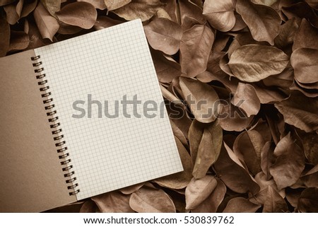 Vintage picture tone of Autumn background. The fallen autumn leaves and notebook on wooden garden table. can used add text message or greeting card.