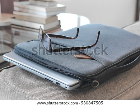 grey laptop case sitting on brown comfortable sofa protects laptop and stylish glasses. good for freelance writer who can write down ideas and prepare his work while traveling