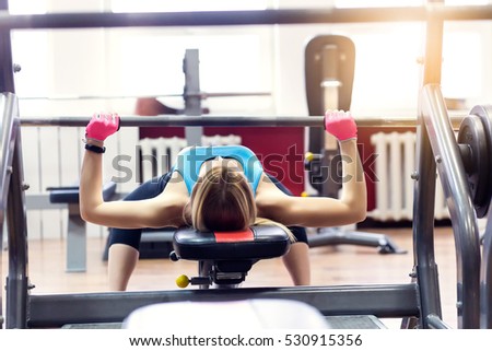 Back view of young adult girl doing bench barbell in gym. Woman with muscular body doing lifting exercise. Fit women do fitness, workout sport concept