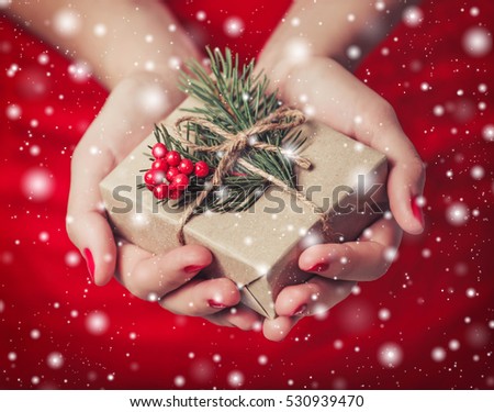 Female hands holding Christmas gift box with branch of fir tree on shiny xmas background. Holiday gift and decoration
