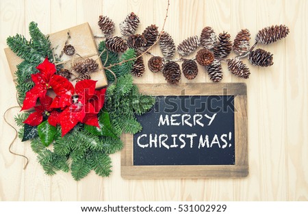 Pine branches with red flowers poinsettia decoration and blackboard on wooden background. Vintage style toned picture
