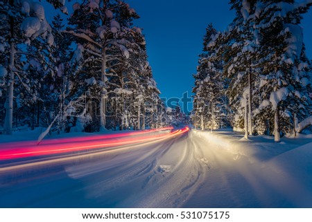Winter Driving - Lights of car and winter road in dark night forest, long exposure