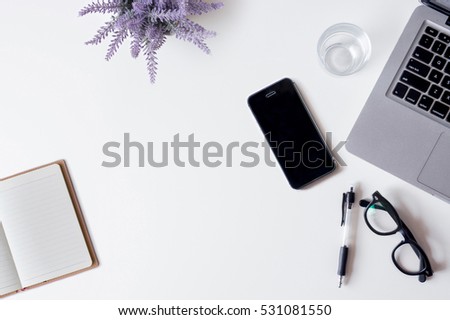 White office desk table with laptop, smartphone, notebook, lavender, and glass. Top view with copy space, flat lay.