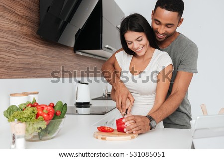Picture of cheerful young couple in the kitchen hugging while cooking.