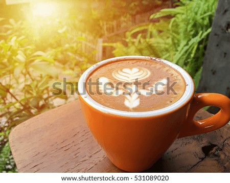 Latte coffee in orange cup with blurred fresh green background