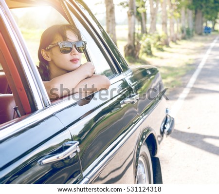 Car woman happy in old  retro vintage car. Young woman driving on road trip on beautiful sunny summer day. Pretty mixed race Asian / Caucasian female model.

