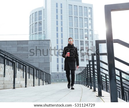 Full length business man in warm clothes with coffee walking near the stairs