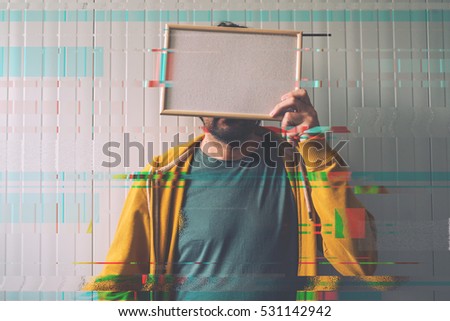 Unrecognizable man posing with blank picture frame over his face as copy space, digital glitch effect added in post production