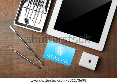 Business card, tablet and dental tools on wooden background. Medical service concept