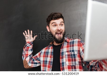 Photo of happy man dressed in shirt in a cage waving to friends at internet while using tablet computer