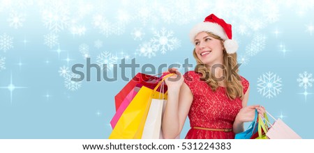 Smiling blonde in santa hat holding shopping bags against snowflakes on blue background