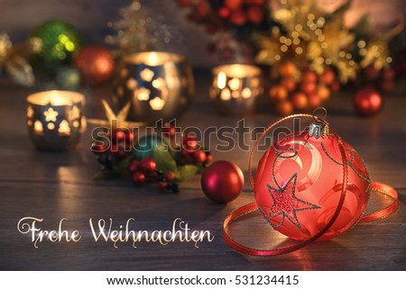 Christmas arrangement on wooden table with baubles, berries and candles. Caption on the picture means "Merry Christmas" in German.