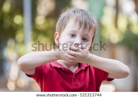 Serious little Caucasian boy closing his mouth with hands. Illustrative image for childhood trauma, child traumatic experience. Psychological assistance, children rescue. Silent cry for help. Stutter Royalty-Free Stock Photo #531313744