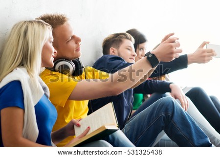 Group of happy students being on a break taking selfie. Focus on a happy girl and boy in headphones. Background is blurry.