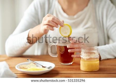 health, traditional medicine and ethnoscience concept - close up of ill woman drinking tea with lemon, honey and ginger at wooden table Royalty-Free Stock Photo #531335296