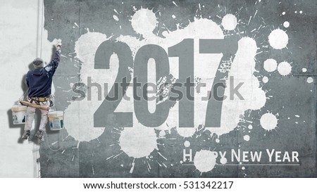 Building painter hanging from harness painting a wall with the words Happy New Year 2017