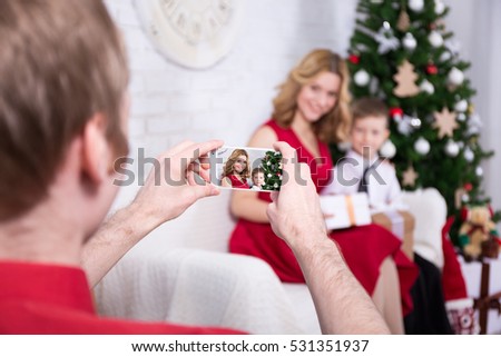 young man taking photo of his wife and son with Christmas tree