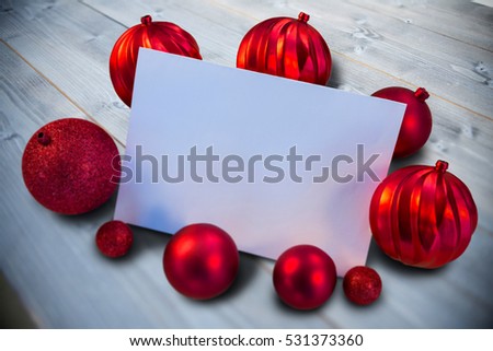 Red christmas baubles surrounding white page against bleached wooden planks background