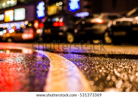 Rainy night in the parking shopping mall, parked cars illuminated advertising signs. Close up view from the level of the dividing line