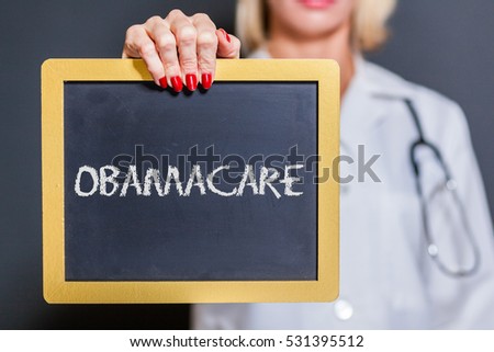 Obamacare Chalkboard Sign Held By Female Doctor In Dark Room.