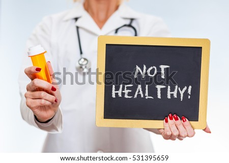 Not Healthy Written On Chalkboard Sign Held By Female Doctor Holding Prescription Bottle.