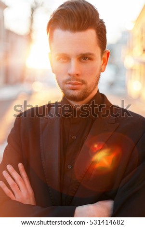 Handsome man with a beard and hairstyle in black elegant suit at sunset