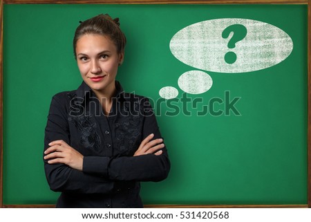 Beautiful young woman teacher (student, business woman) in classical dress standing near a blackboard with the question