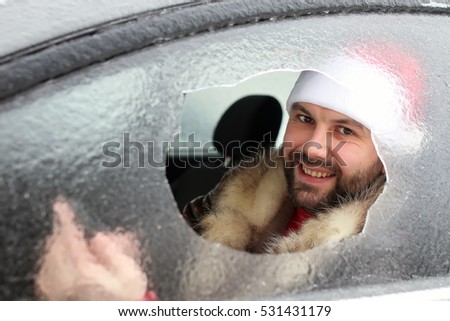 bearded man in a red cap of Santa Claus in a car with broken glass