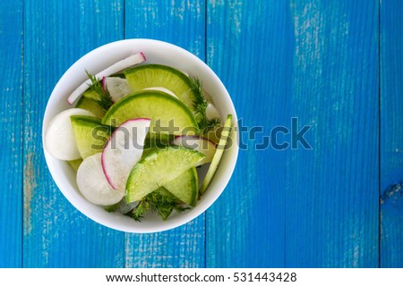 Salad of radish of different varieties (daikon, green, Chinese red) chopped slices, flavored with sunflower oil in a white bowl on a blue wooden background. The top view